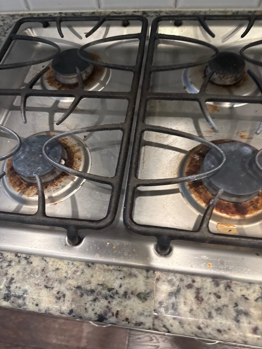 A gas cooktop before cleaning, with burnt-on residue around every burner