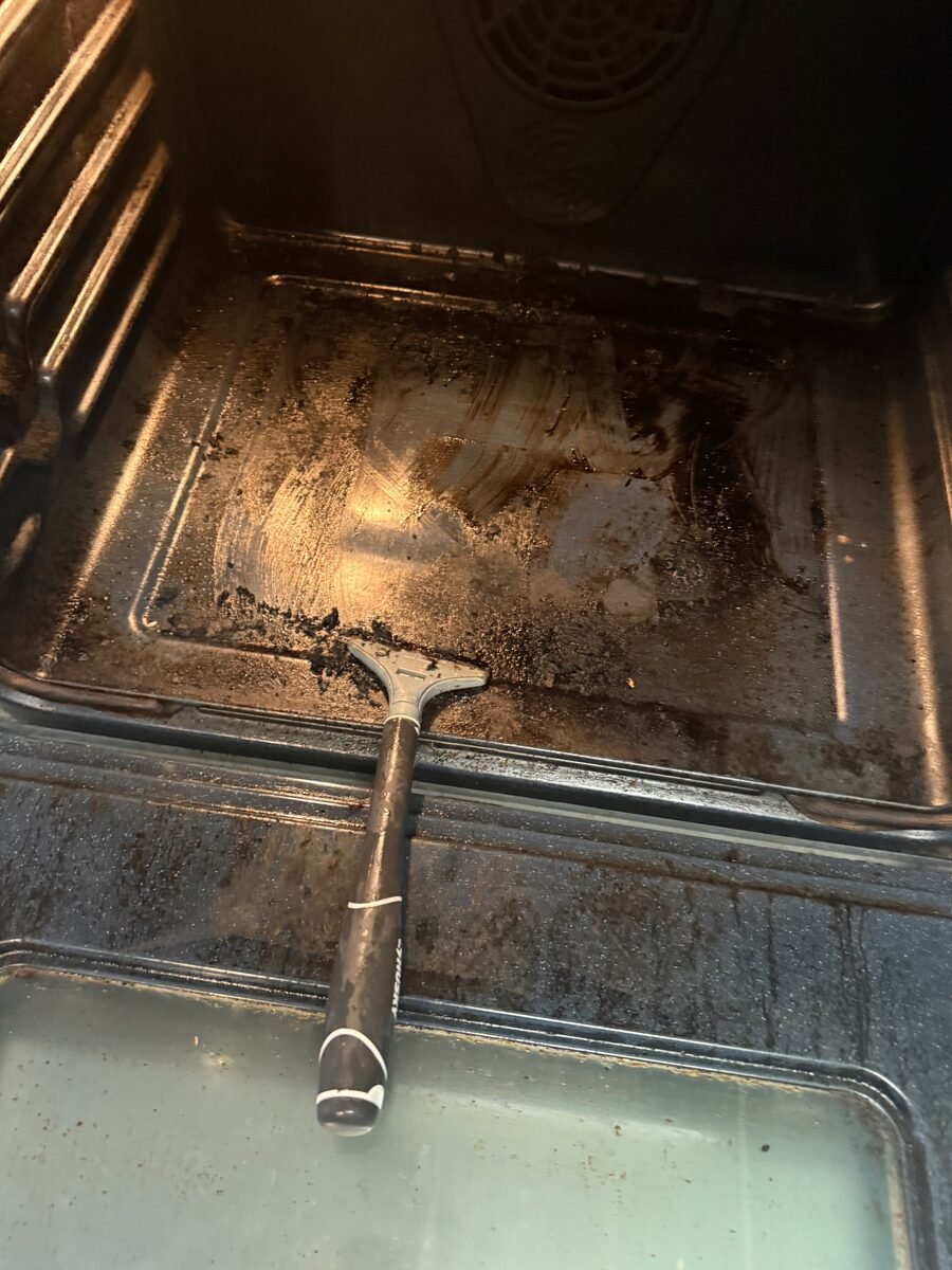 An oven interior before cleaning, with baked-on grease across the floor of the cavity