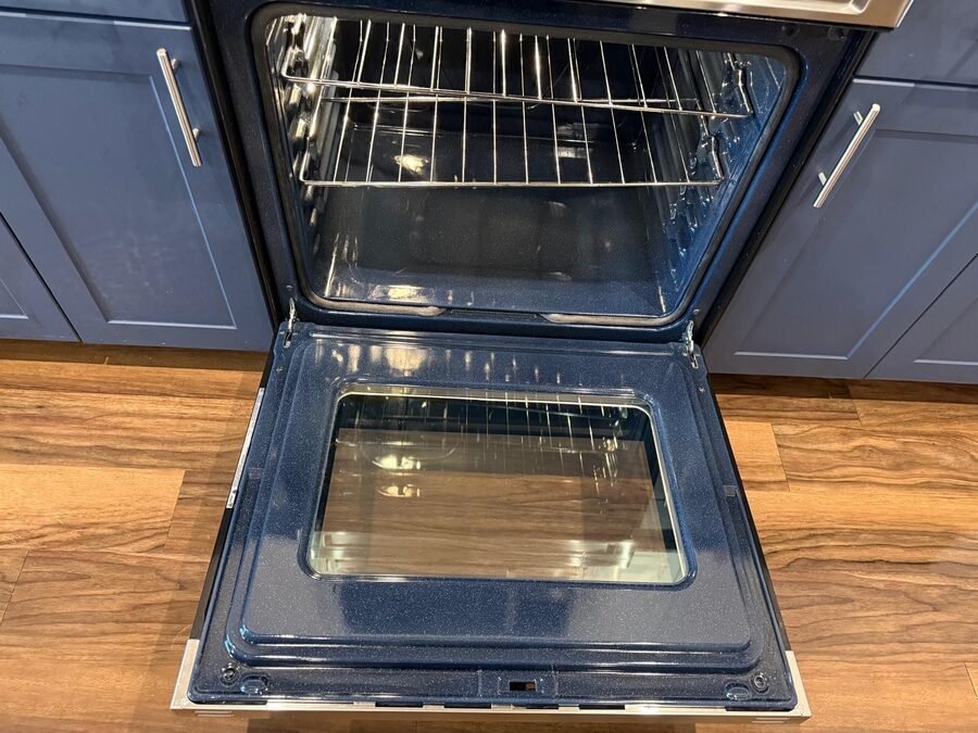 An oven standing open with clean racks in a navy-cabinet kitchen